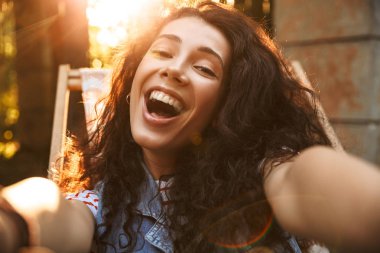 Kamera gülerek selfie yapmak imge-in mutlu genç güzel kıvırcık kadın açık havada park.