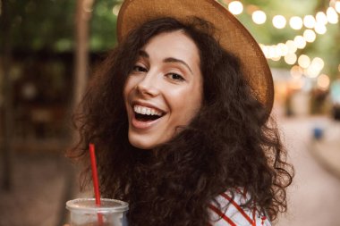 Güzel esmer kadın 18-20 giyen yaz hasır şapka ile renkli lambalar Park'ta dinlenme sırasında plastik bardak soğuk çay içme closeup fotoğraf