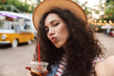 Görüntü şık güzel kadının 18-20 yaz hasır şapka gülümseyen ve plastik bardak selfie fotoğraf çekerken açık soğuk çay içme kıvırcık kumral