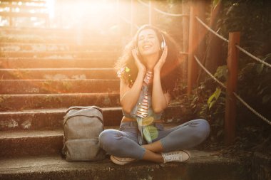 Görüntü oturan sevimli genç kadının açık havada park kulaklık ile müzik dinleme adımları.