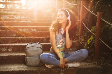 Görüntü oturan sevimli genç kadının açık havada park kulaklık ile müzik dinleme adımları.