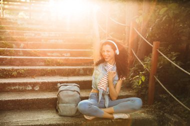 Kazanan jest yapmak imge-in açık havada kulaklık ile müzik Park adımlar üzerinde oturan sevimli genç kadın.