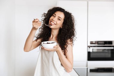 Tatlı kahvaltı mutfak sahip ve sütlü çikolata granola yemek genç kıvırcık kadın 20'li yaşlarda giyen ipek eğlence giyim fotoğrafı