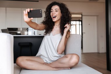 Genç ve güzel kadın ipek eğlence giyim rahat evde kanepede otururken cep telefonundan selfie fotoğraf çekme