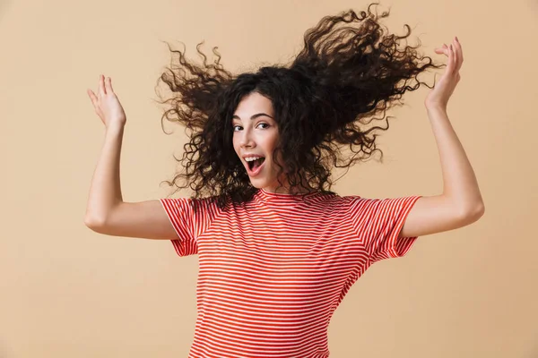 Görüntü şirin mutlu genç kadının saçını sallayarak bej duvar arka plan üzerinde izole ayakta.