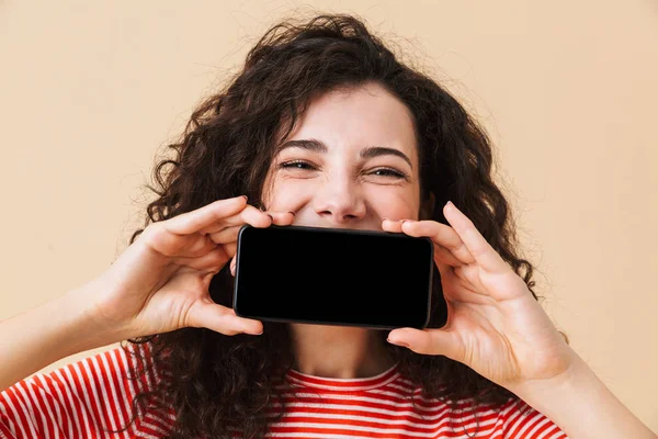 Ekran cep telefonu tarafından ağız kapsayan gösterilen bej renkli arka plan üzerinde izole duran sevimli genç kıvırcık kadın görüntüsünü.