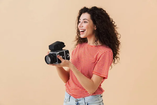 Image of pretty young curly woman photographer isolated over beige background holding camera.