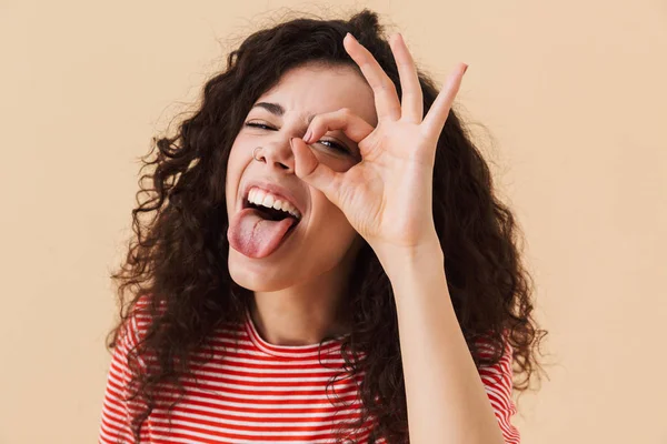 İyi jest yapmak imge-in duygusal genç kıvırcık kadın kamera seyir bej renkli arka plan üzerinde izole.