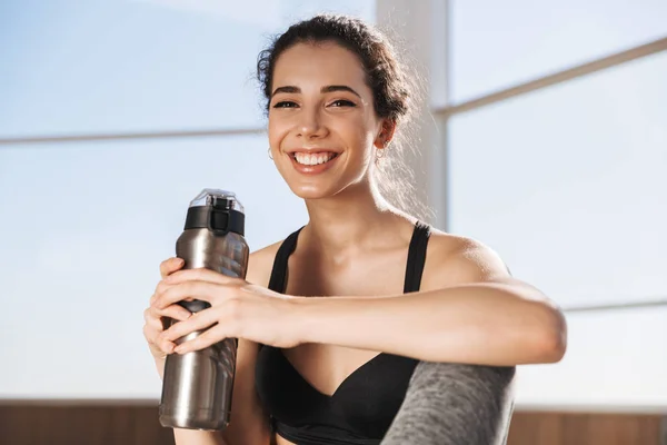 Smiling Young Sportswoman Holding Water Bottle While Sitting Window Indoors — Stock Photo, Image