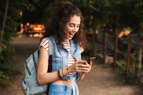 Φωτογραφία Χαρά Γυναίκα Φορώντας Backpack Χαμογελώντας Και Κοιτάζοντας Smartphone Ενώ — Φωτογραφία Αρχείου