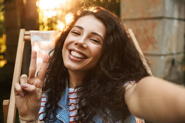 Kamera tarafından selfie yapmak imge-in mutlu güzel kıvırcık olan kadın barış hareketle park açık havada.
