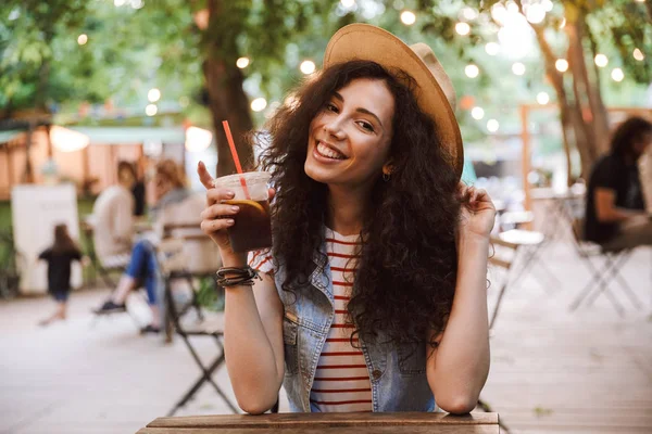 Görüntü güzel mutlu kadın 18-20 giyen yaz hasır şapka park kafede istirahat ederken plastik bardak soğuk çay içme