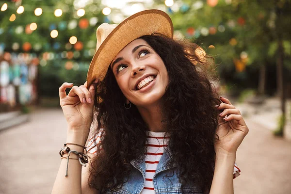 Şık sevimli kadın 18-20 gülüyor ve hasır şapkasına renkli lambalar arka plan ile hipster spot ya da modern park içinde kalan süre dokunaklı kıvırcık kumral fotoğrafı
