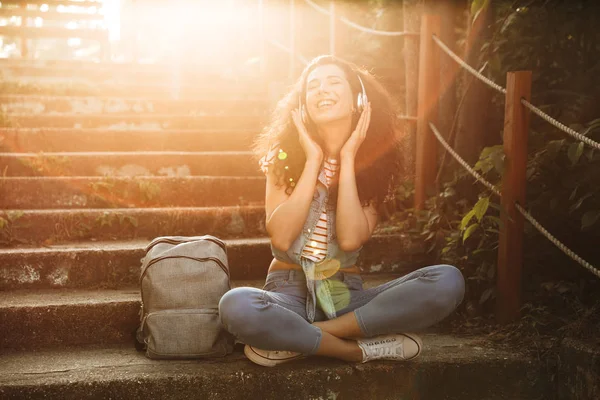 Görüntü oturan sevimli genç kadının açık havada park kulaklık ile müzik dinleme adımları.
