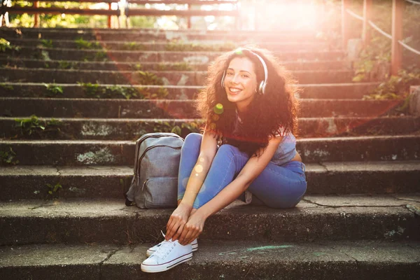 Görüntü oturan sevimli genç kadının açık havada park müzik dinleme kamera seyir kulaklıklar ile adım..