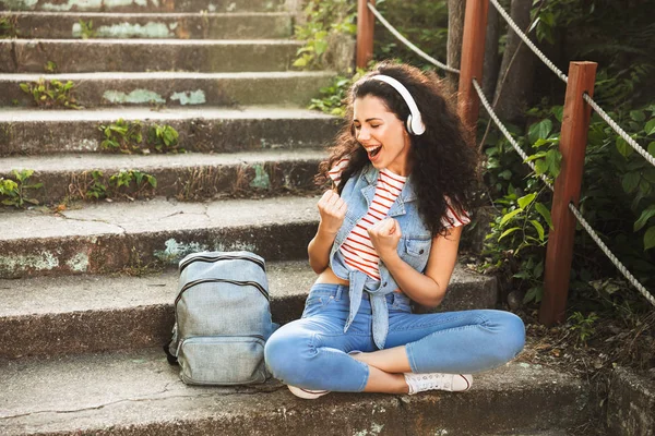 Kazanan jest yapmak imge-in açık havada kulaklık ile müzik Park adımlar üzerinde oturan sevimli genç kadın.