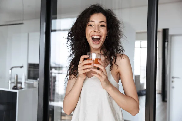 照片的兴奋卷曲的女人与长的黑发微笑着在你 而在单位举行橙汁玻璃 — 图库照片