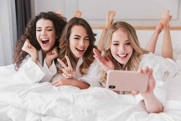 Üç Avrupa çok güzel kadınlar 20'li yaşlarda evde lüks yatak odasında yalan ve selfie fotoğraf üstünde hareket eden telefon sırasında gelin duş alarak beyaz bornoz giyiyor