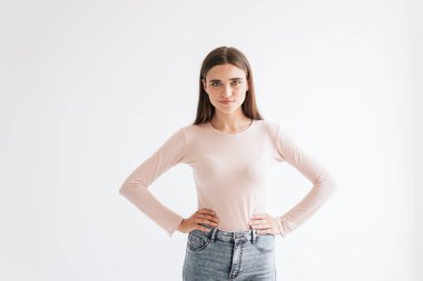 Beyaz arka plan üzerinde izole kalça kollarda ayakta rahat kıyafetler içinde kendine güvenen genç esmer kız portresi