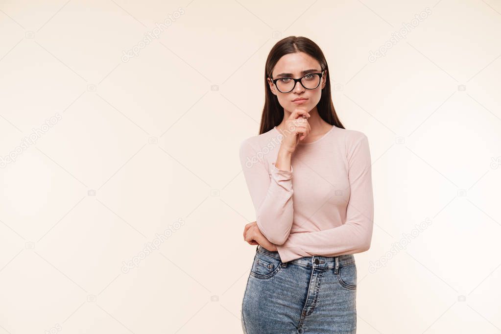 Portrait of a confident young brunette woman in eyeglasses looking at camera isolated over pink background