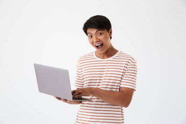 Neşeli bir genç Asyalı adam üzerinde beyaz izole ayakta iken dizüstü bilgisayar kullanan portresi