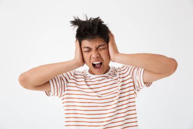 Kızgın tahriş Asya adam çizgili giyen 20s fotoğrafı çığlık ve gürültü nedeniyle kulakları kapsayan t-shirt beyaz arka plan üzerinde izole.