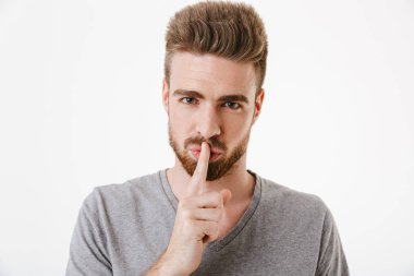 Beyaz arka plan üzerinde izole sessizlik jest gösterilen ciddi bir genç sakallı adam portresi