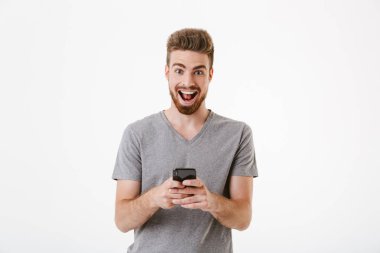 Cep telefonu kullaranarak beyaz duvar arka plan üzerinde izole ayakta mutlu yakışıklı genç adam görüntüsü. Görünümlü kamera.