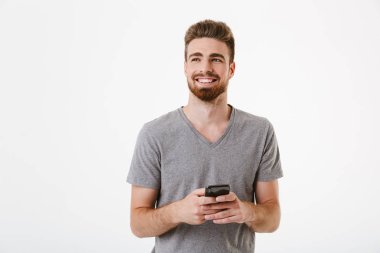 Cep telefonu kullaranarak beyaz duvar arka plan üzerinde izole ayakta mutlu yakışıklı genç adam görüntüsünü.