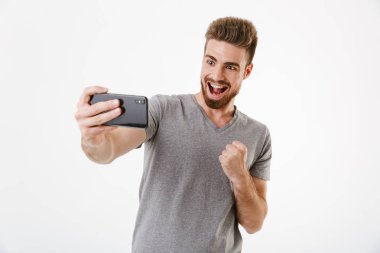 Kazanan jest yapmak imge-in heyecanlı genç adam beyaz duvar arka plan oyun oyunlar üzerinden cep telefonuyla izole ayakta.