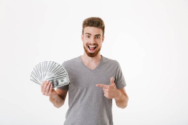 Heyecanlı neşeli genç adam para işaret tutan beyaz duvar arka plan üzerinde izole ayakta görüntüsünü.