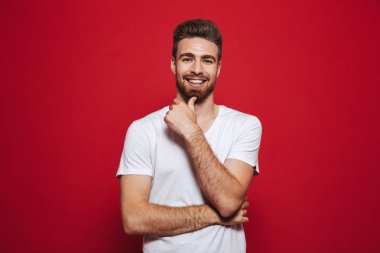 Neşeli yakışıklı genç izole kırmızı arka plan üzerinde beyaz t-shirt görünümlü kamera görüntüsünü.