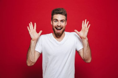 Heyecanlı yakışıklı genç izole kırmızı arka plan üzerinde beyaz t-shirt görünümlü kamera görüntüsünü.