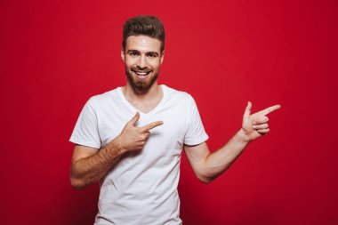 Mutlu yakışıklı genç beyaz t-shirt kırmızı arka plan işaret içinde izole içinde görüntü.