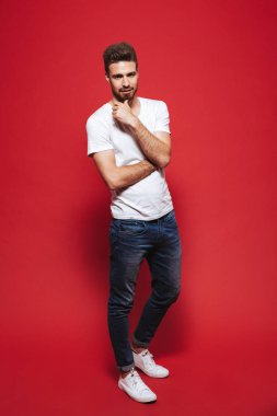 Kendine güvenen genç sakallı adam kırmızı arka plan üzerinde izole ayakta iken poz tam uzunlukta portresi