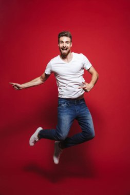 Mutlu genç sakallı adam işaret eden bir parmağa iken başarı kutluyor ve atlama üzerinde kırmızı arka plan izole kopya alanı, tam uzunlukta portresi