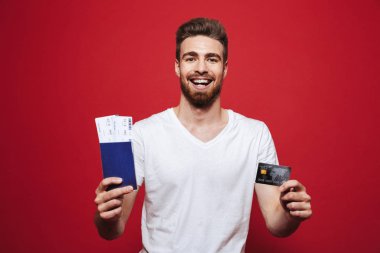 Bilet ve gösteren plastik kredi kartı üzerinde kırmızı arka plan izole neşeli Genç sakallı adam holding Passport'a portresi