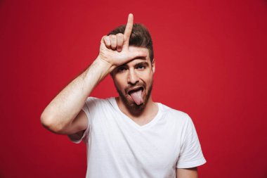 Alnına parmak dayanabiliyor ve kırmızı arka plan üzerinde izole dil yapışkanlık dışarı bir komik Genç sakallı bir adam portresi