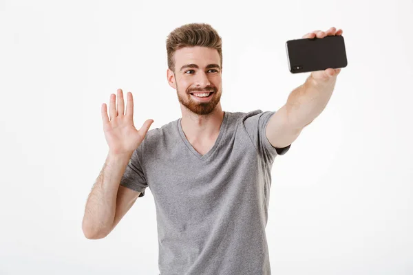 白い壁の背景に分離立って幸せのハンサムな若い男のイメージになる携帯電話を振ることによって話している Selfie — ストック写真