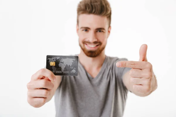 クレジット カードのポイントを保持している白い壁の背景に分離立って幸せな陽気な若い男のイメージ — ストック写真
