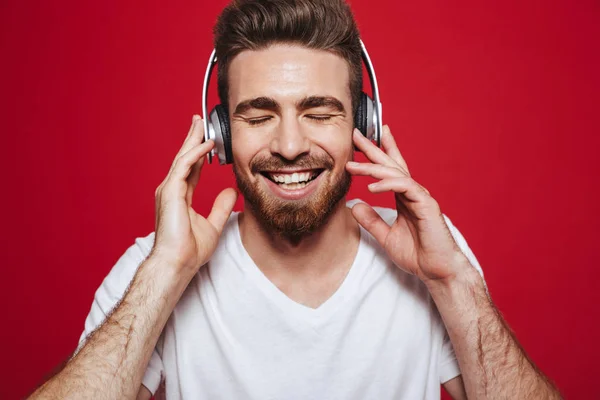 英俊的情绪年轻人在白色 T恤的照片听音乐与耳机隔离在红色背景 — 图库照片