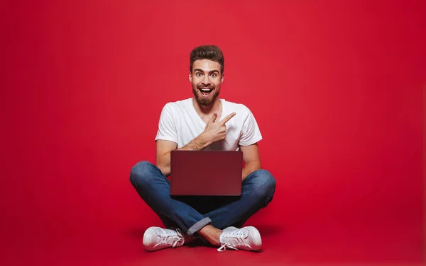 Retrato Jovem Barbudo Feliz Apontando Para Espaço Cópia Enquanto Sentado — Fotografia de Stock