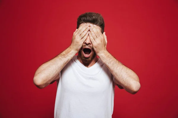 Портрет Шокированного Молодого Бородатого Мужчины Закрывающего Лицо Руками Красном Фоне — стоковое фото
