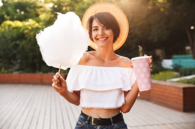 Pamuk şeker yeme ve içme plastik bir kap parkta gelen yaz elbise giymiş genç kız gülümseyerek