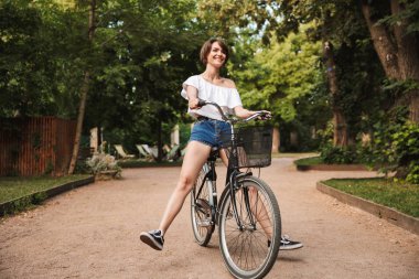 Genç kız parkta bir bisiklet sürme yaz giysileri gülümseyen