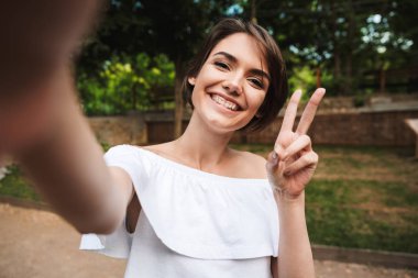 Genç kız gösteren barış hareketi parkta bir selfie çekerken gülümseyen