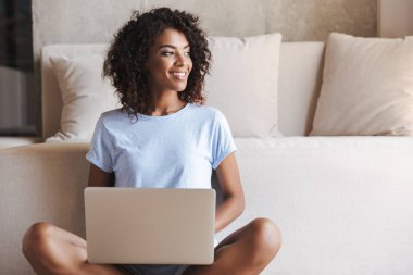 Evde bir kanepede otururken dizüstü bilgisayar kullanan mutlu Afrika kadın