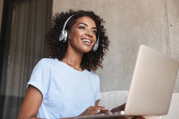 Sorridente Donna Africana Cuffia Utilizzando Computer Portatile Mentre Seduto Divano — Foto Stock