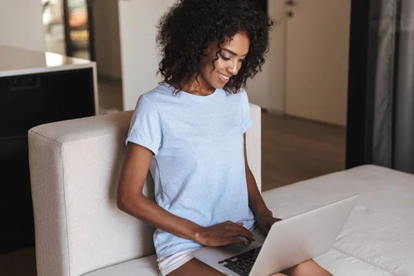 Lachende Afrikaanse Vrouw Met Laptopcomputer Zittend Een Bank Thuis — Stockfoto