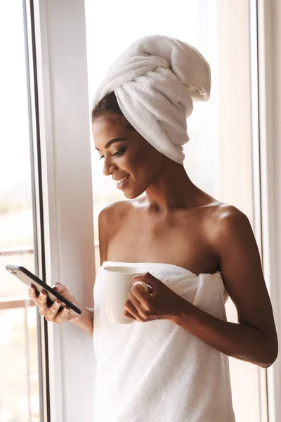 Ελκυστική Γυναίκα Αφρικανική Τυλιγμένο Μια Πετσέτα Χρησιμοποιώντας Κινητό Τηλέφωνο Ενώ — Φωτογραφία Αρχείου